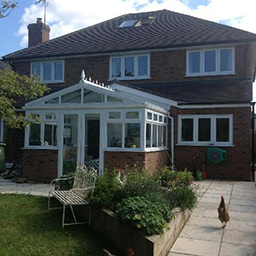 a conservatory on the back of a house leading to a garden with a chicken running in it